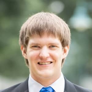 Picture of me in a suit, donning a tie with a fancy knot; blurred foliage in the background